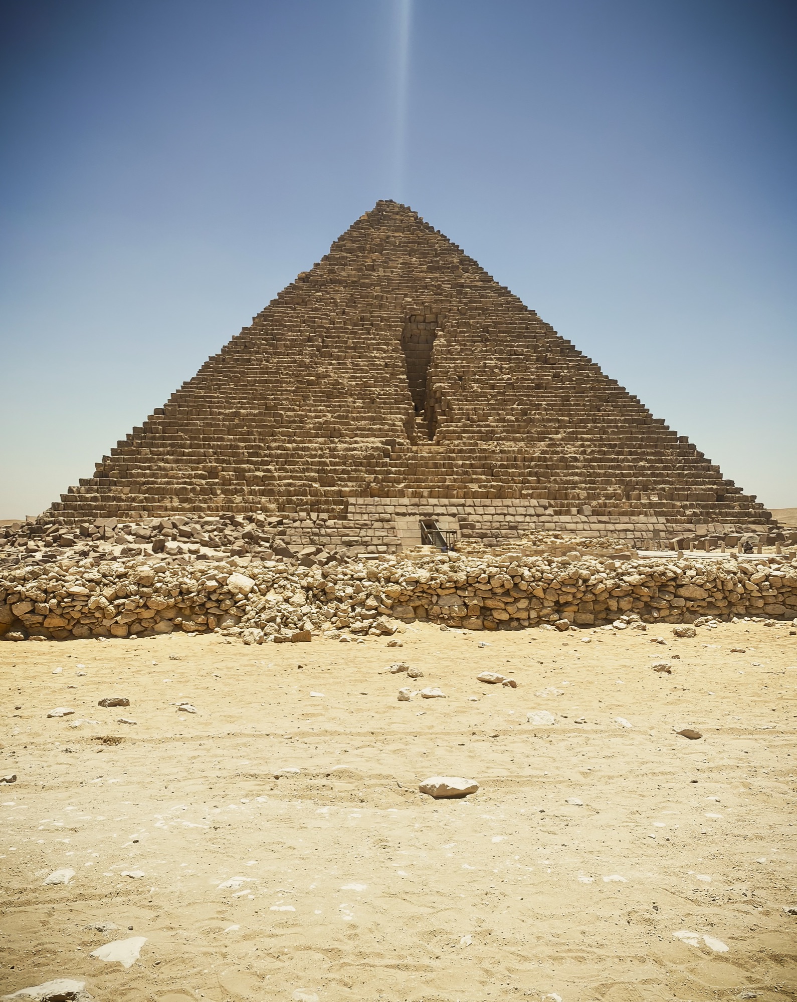The Great Pyramid of Giza rising against a clear blue sky, a lone figure at its base for scale.