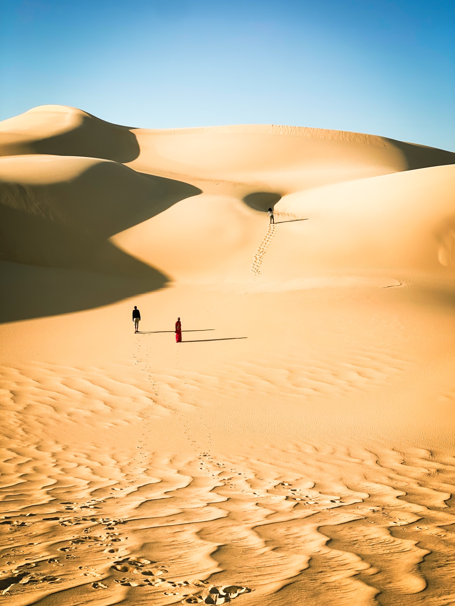 Sweeping golden dunes of the Siwa desert, two tiny figures crossing the sand for scale.